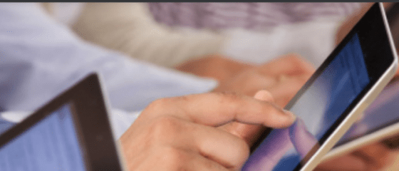 The hands of a person hovered over a tablet, seeming to be in a classroom setting