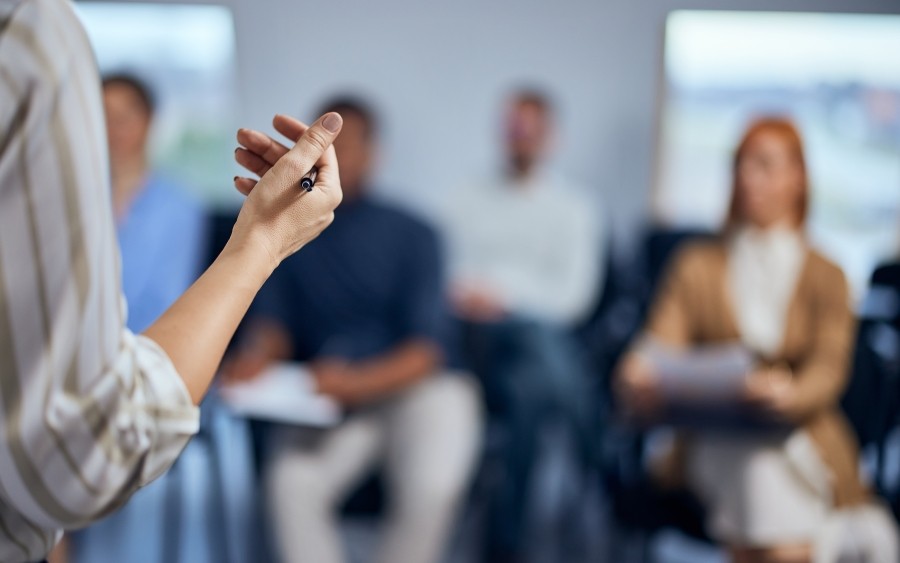 A cropped image of a person facing an audience of adult students. Their gesturing hand is in focus. 